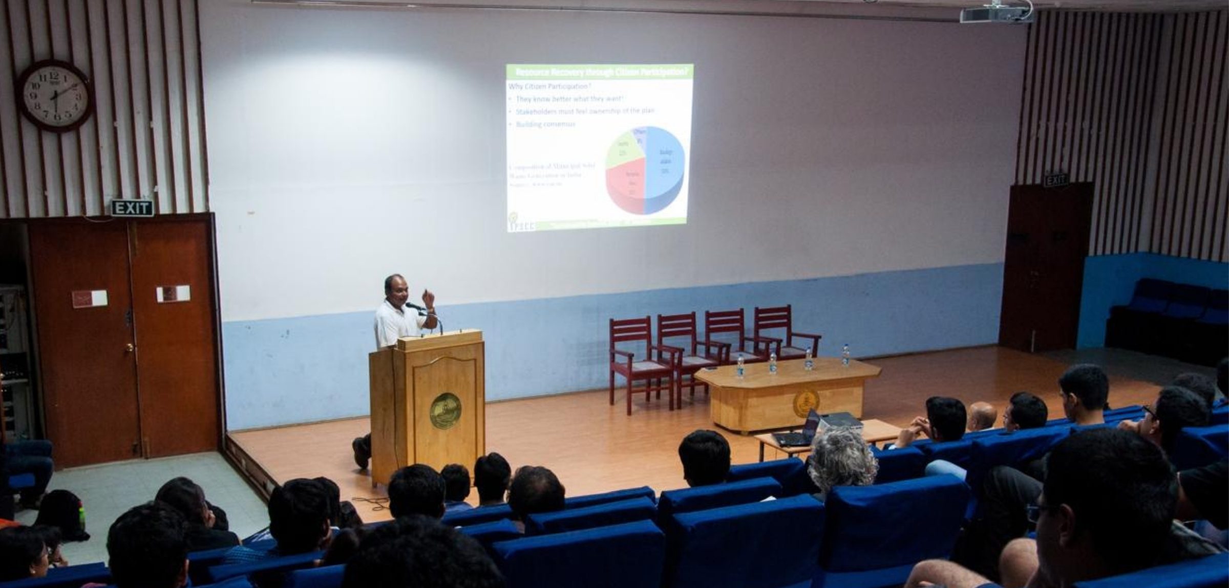 A speaker addresses a full auditorium at the Sustainability Summit 2015, presenting a slide on resource recovery through citizen participation
